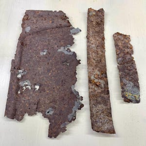 Peut inclure: Plusieurs morceaux de métal rouillé et vieilli. Le plus grand est de forme irrégulière, avec des bords déchirés. Deux bandes rectangulaires de longueurs différentes sont également présentes, toutes montrant des signes de corrosion.