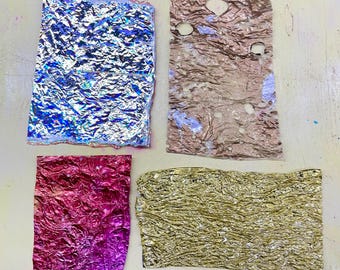 Puede incluir: Cuatro trozos de papel de aluminio arrugado en varios colores. La parte superior izquierda es azul y plateada, la superior derecha es marrón, la inferior izquierda es rosa y morada y la inferior derecha es dorada. El papel de aluminio tiene un aspecto texturizado y arrugado.