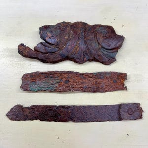 Peut inclure: Trois pièces métalliques rouillées et usées. La pièce supérieure présente un motif décoratif en forme de volute. La pièce du milieu est une longue bande rectangulaire. La pièce inférieure est une bande plate et rectangulaire avec une extrémité arrondie.