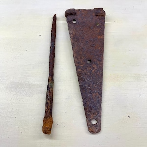 Peut inclure: Deux objets métalliques anciens et fortement rouillés. L'un est un long clou fin, l'autre une charnière triangulaire avec trois trous. Les deux articles présentent une couleur brun foncé, indiquant un âge important et une exposition aux éléments.