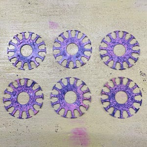 Puede incluir: Seis piezas decorativas circulares con un agujero central y radios. Las piezas tienen un patrón moteado púrpura y rosa. El fondo es una superficie de color amarillo verdoso claro.