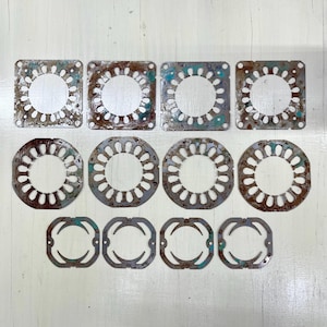 Peut inclure: Dix composants métalliques patinés avec des motifs découpés complexes. Les pièces sont de formes variées, notamment carrées, circulaires et rectangulaires arrondis, et présentent un mélange de rouille et de patine de couleur sarcelle. L'arrangement suggère un thème mécanique ou industriel.
