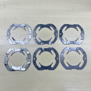 May include: Six identical, silver-colored metal rings with an oval shape and a series of small holes around the outer edge. Each ring has a curved, open section in the center. The rings are arranged in two rows of three.