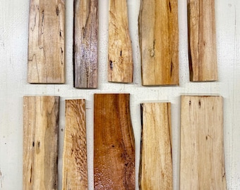 May include: An overhead shot of eleven rectangular wooden planks with varying shades of brown and tan. The planks have natural edges and visible wood grain, showcasing the natural beauty of the wood. Some planks have a glossy finish.