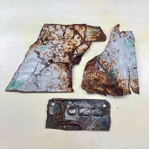 Peut inclure: Quatre morceaux de métal vieilli avec de la rouille et une patine verte. La plus grande pièce est de forme irrégulière avec un bord argenté et vert. Une pièce rectangulaire porte le mot "OZZ" en relief.
