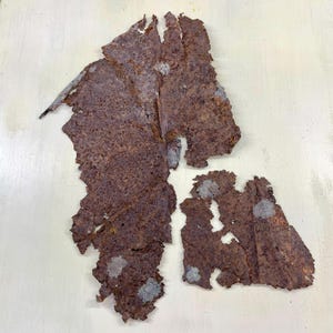 May include: Close-up of several pieces of weathered, rusty metal with irregular edges. The metal has a dark brown color with patches of lighter gray and white. The pieces appear torn or broken, suggesting age and exposure to the elements.