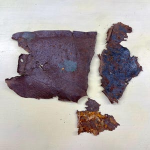 Peut inclure: Gros plan de plusieurs morceaux de métal rouillé et vieilli. Les fragments de métal sont de formes et de tailles variées, avec une couleur brun-rouge foncé et des zones d'oxydation bleu-vert. Les pièces sont disposées sur une surface de couleur claire.