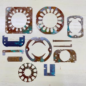 May include: A collection of irregularly shaped, rusted metal pieces with holes and cut-out designs. The pieces show shades of brown, blue, and green, suggesting age and exposure to the elements. The arrangement includes circular, rectangular, and other geometric forms.