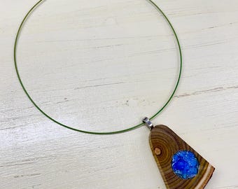 May include: A wooden pendant necklace with a blue stone inlay. The pendant is a triangular shape with a natural wood grain pattern. The necklace has a green wire and a silver clasp.