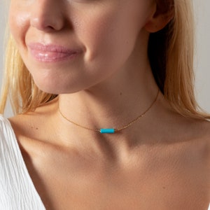 a woman wearing a necklace with a turquoise bar on it
