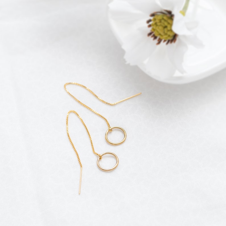 a pair of gold earrings sitting on top of a white table