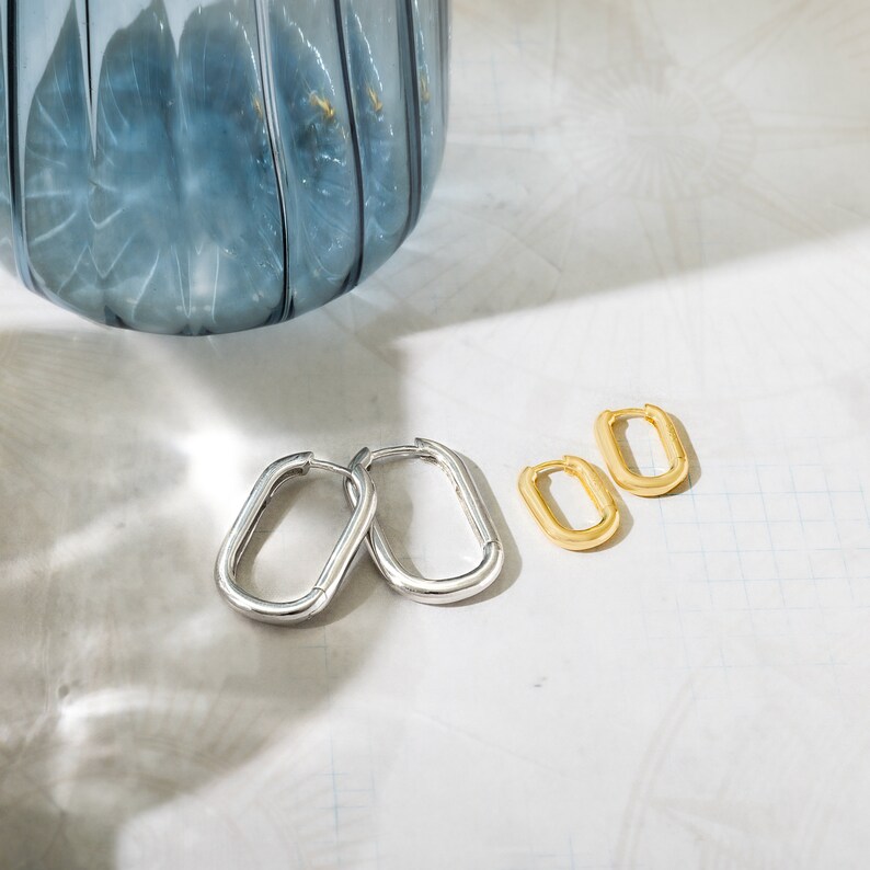 a pair of silver and gold earrings next to a blue vase