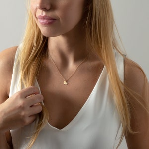 a woman in a white top is holding a necklace