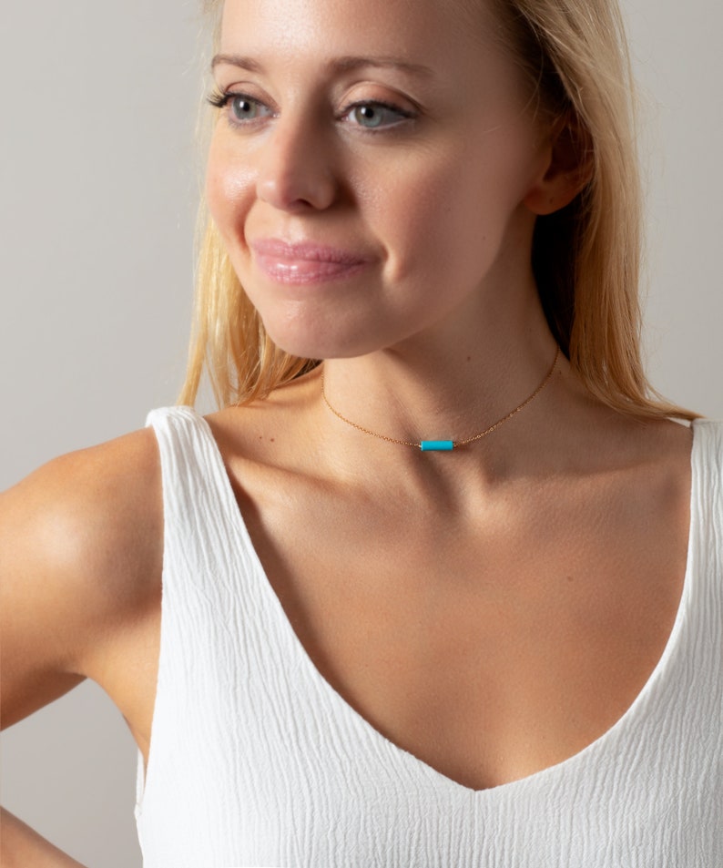 a woman wearing a white top and a blue necklace