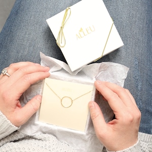 a woman holding a box with a necklace in it
