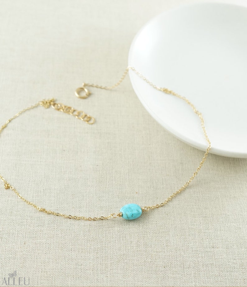 a gold chain bracelet with a turquoise bead