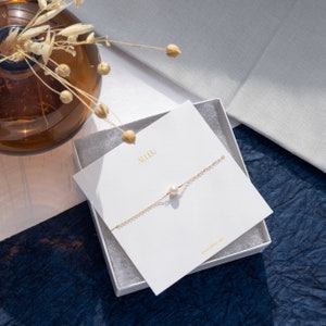 a white box with a necklace on it next to a vase with flowers