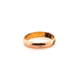 May include: A solid gold band ring with a smooth, polished surface and a rounded profile. The metal exhibits a warm, metallic yellow hue with subtle variations in tone across the exterior surface of the circular jewelry piece.