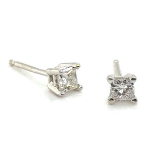 May include: Two small, square-cut diamond stud earrings. The diamonds are set in a silver or white gold setting. The earrings are displayed on a white background.