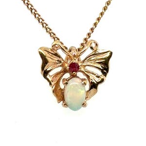 May include: A gold-toned necklace featuring a butterfly-shaped pendant. The pendant is set with a small, round, deep red gemstone at the top and a larger, oval-shaped, iridescent white opal gemstone at the bottom, suspended on a delicate chain.