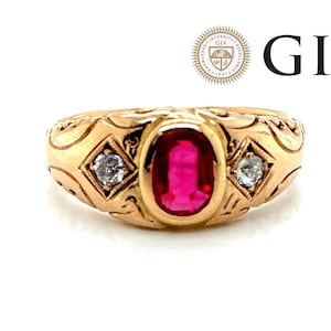 May include: A gold ring with an oval ruby center stone and two smaller diamonds. The ring has an ornate, engraved design. The GIA logo and text are visible in the background.
