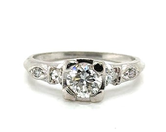 May include: A silver engagement ring with a large, round, clear diamond center stone. Two smaller diamonds flank the center stone on each side. The ring is set against a white background.