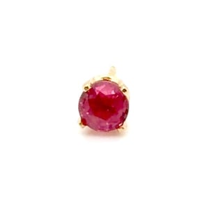 May include: A round, faceted, deep pink gemstone set in a gold prong setting. The stone is circular with a brilliant cut, displaying multiple reflective surfaces. The metal prongs secure the gemstone at the base, creating a small stud earring.