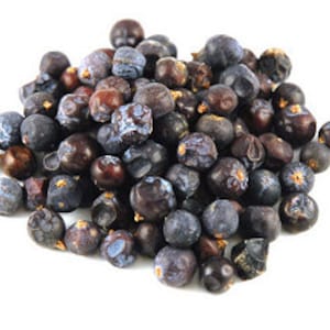 May include: A close-up of a pile of dried juniper berries. The berries are a mix of dark blue and brown, with a wrinkled texture. They are clustered together against a white backdrop. Juniper berries are a key ingredient in gin and are used in cooking.