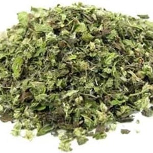 May include: A pile of dried, chopped green herbs, possibly for culinary or medicinal use. The herbs have a mix of green and brown hues, with a slightly textured appearance. The image is set against a plain white background.