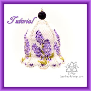 Op de afbeelding: Een witte kralenbel ornament met een paars bloemenontwerp. De bel heeft een gegolfde rand en een kleine zwarte kraal aan de bovenkant. Het ornament is gelabeld "Iceni Bead Design".
