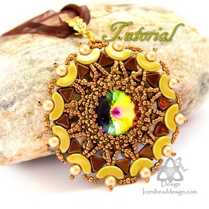 May include: A gold, brown, and green beaded pendant with a large iridescent crystal in the center. The pendant is hanging from a brown ribbon and is resting on a rock.
