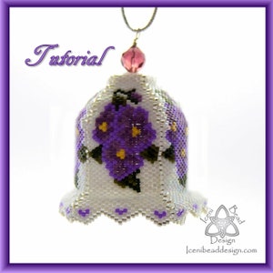 May include: A white beaded bell ornament with a purple flower design. The bell is hanging from a silver chain with a pink crystal bead at the top. The ornament is labeled "Iceni Bead Design".