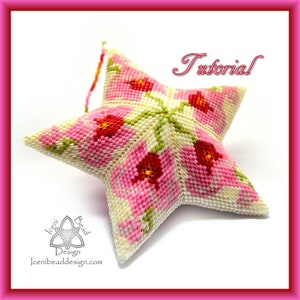 May include: A pink and white beaded star ornament with a floral design. The star is 3-dimensional and has a textured surface. The ornament is labeled "Tutorial".