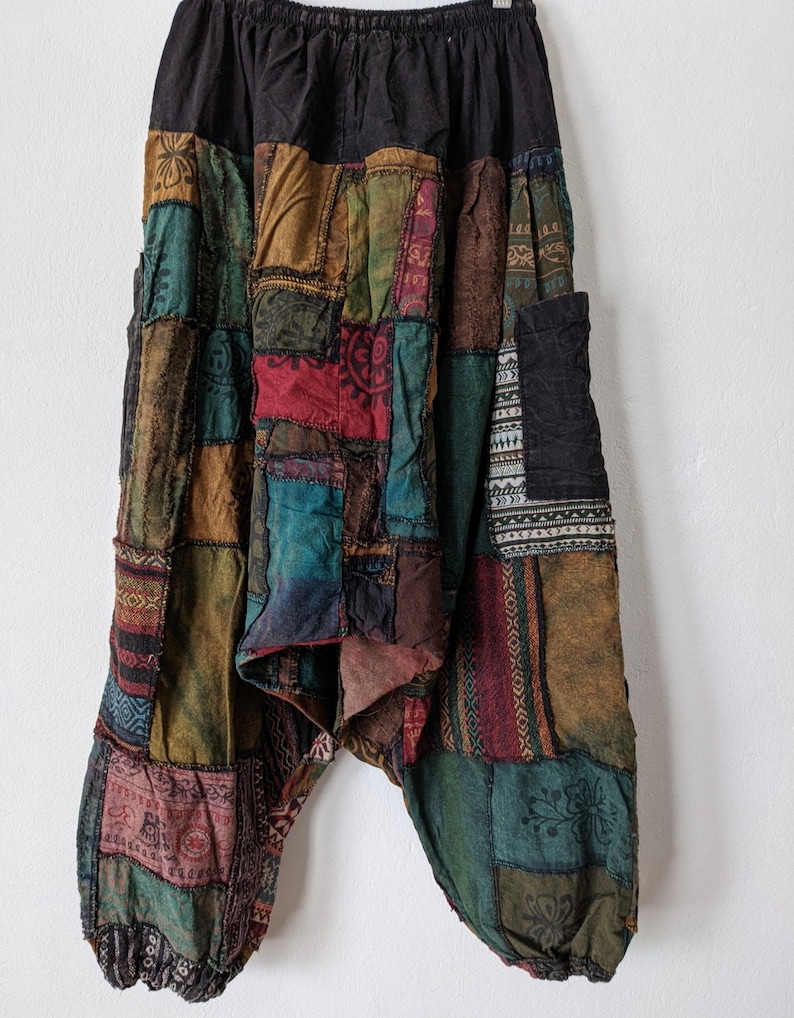 Może przedstawiać: Spodnie harem w stylu patchwork z czarną elastyczną talią. Spodnie posiadają r&oacute;żnorodne kolorowe łaty materiału w odcieniach zieleni, czerwieni, brązu i niebieskiego. Luźne spodnie mają swobodny, bohemiczny styl.
