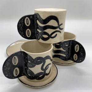 Puede incluir: Un juego de tres tazas de cerámica con un acabado moteado y mate. Las tazas son de color crema, gris claro y gris oscuro. Cada taza tiene un diseño simple y minimalista, ideal para café o té.