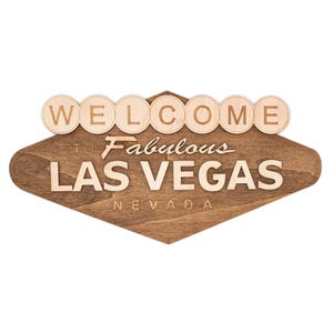 May include: Wooden sign with the words "WELCOME TO Fabulous LAS VEGAS NEVADA". The sign has a diamond shape with a dark brown stain and light brown lettering. The word "WELCOME" is in individual circles.