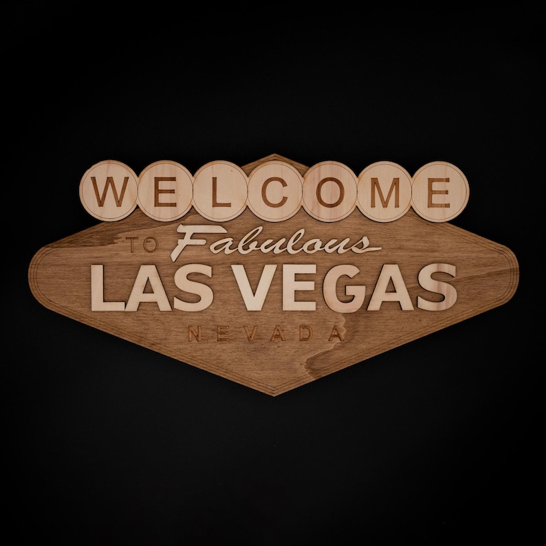 May include: Wooden sign featuring the iconic "Welcome to Fabulous Las Vegas Nevada" design. The sign is made of light brown wood with the text in a lighter shade. The word "WELCOME" is in individual circular letters.