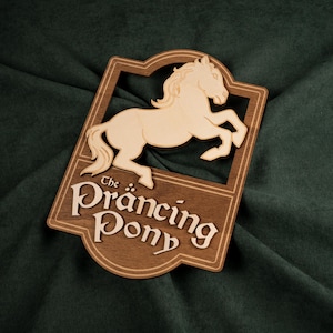 Peut inclure: Panneau en bois représentant un cheval cabré dans un cadre rectangulaire. Le cheval et le lettrage sont de couleur claire, tandis que le fond est en bois plus foncé. Le texte "The Prancing Pony" est affiché en dessous.