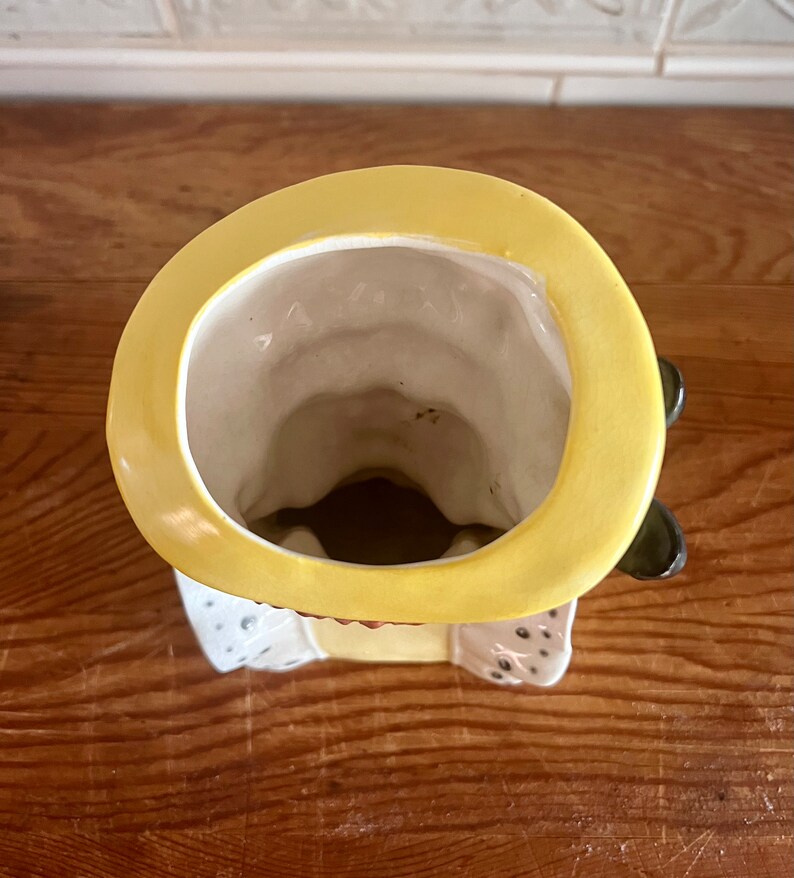 Pu&ograve; includere: Un vaso da fiori in ceramica a forma di persona con un cappello giallo. Il vaso ha una smaltatura bianca ed &egrave; decorato con dettagli marroni e neri. Il vaso ha un'ampia apertura nella parte superiore per la semina.