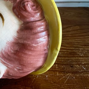 Pu&ograve; includere: Una statuetta in ceramica di una donna con un cappello giallo e capelli rosa. La statuetta &egrave; seduta e ha un viso dettagliato.