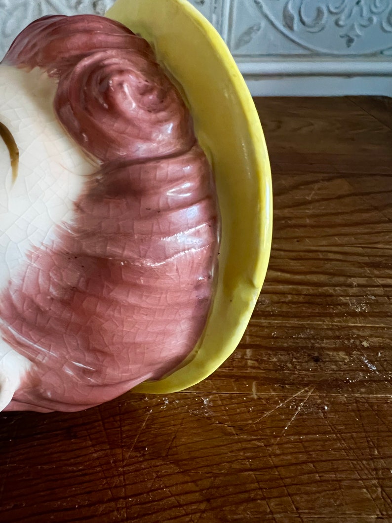 Pu&ograve; includere: Una statuetta in ceramica di una donna con un cappello giallo e capelli rosa. La statuetta &egrave; seduta e ha un viso dettagliato.