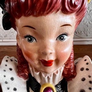 Pu&ograve; includere: Un vaso da fiori in ceramica vintage a forma di busto di donna. Il vaso &egrave; dipinto con un motivo a pois bianchi e neri e presenta un colletto bianco e nero con un accento di gioiello dorato e viola. La donna ha i capelli rossi e un vestito bianco e nero.