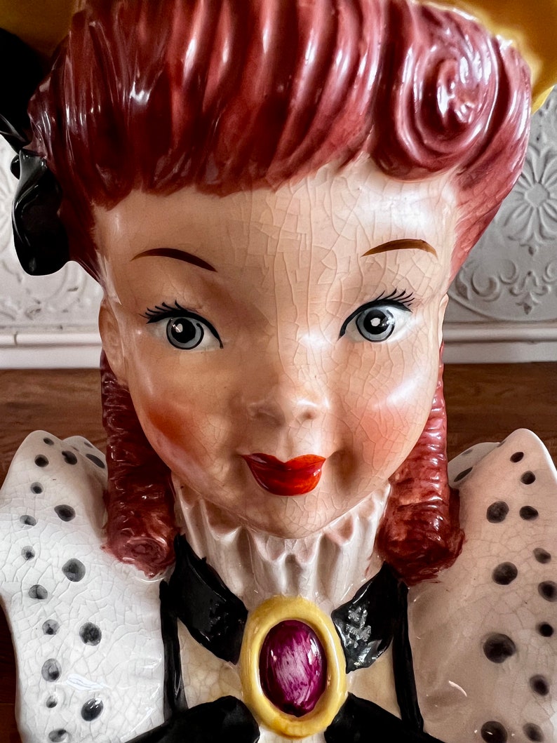 Pu&ograve; includere: Un vaso da fiori in ceramica vintage a forma di busto di donna. Il vaso &egrave; dipinto con un motivo a pois bianchi e neri e presenta un colletto bianco e nero con un accento di gioiello dorato e viola. La donna ha i capelli rossi e un vestito bianco e nero.