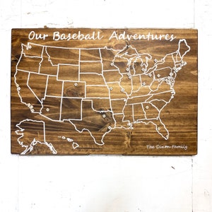 May include: A wooden map of the United States with a white outline of the country and baseballs marking locations. The text "Our Baseball Adventures" is at the top of the map and "The Dixon Family" is at the bottom.