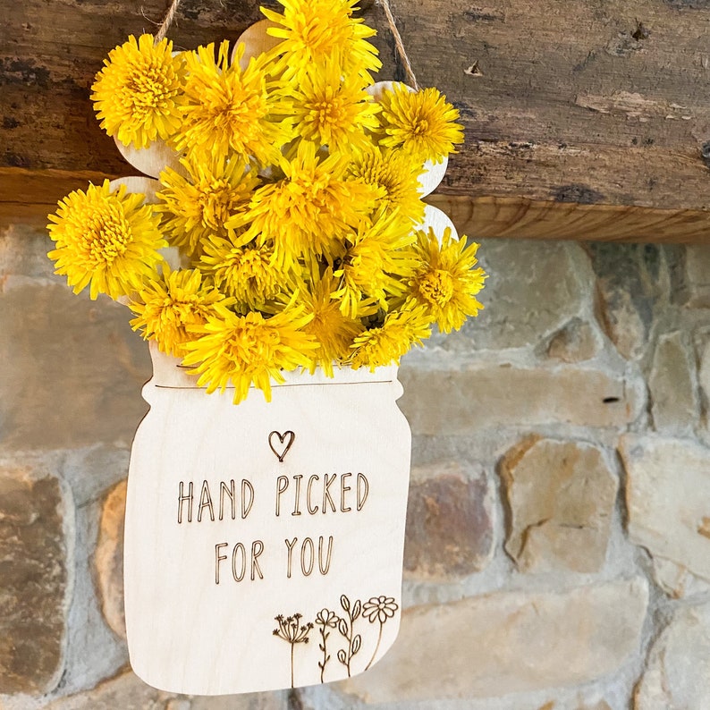May include: A wooden sign shaped like a mason jar with a bunch of yellow dandelions inside. The sign says "Hand Picked For You" with a small heart above the text.