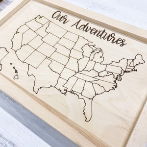 May include: A wooden map of the United States with the text "Our Adventures" at the top. The map is divided into states and is ready to be marked with pins.