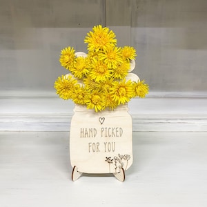 May include: A wooden cutout of a mason jar with a bouquet of yellow dandelion flowers. The jar has a heart and the text "Hand Picked For You" on it.