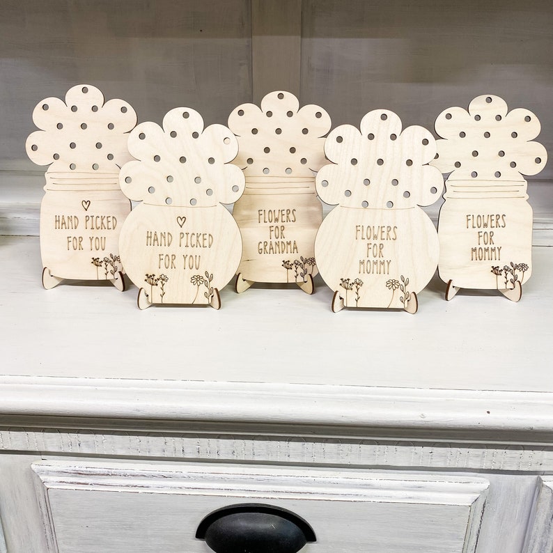 May include: Five wooden flower pot stands with different messages. The messages are "Hand Picked For You", "Hand Picked For You", "Flowers For Grandma", "Flowers For Mommy", and "Flowers For Mommy".