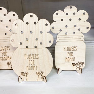 May include: Three wooden flower pot ornaments with holes for inserting flowers. The pots are decorated with the text "Flowers for Grandma", "Flowers for Mommy", and "Flowers for Mommy".