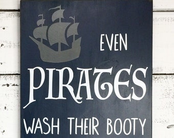 May include: A dark blue wooden sign with white text that reads "Even Pirates Wash Their Booty". A gray silhouette of a pirate ship is in the top left corner of the sign.